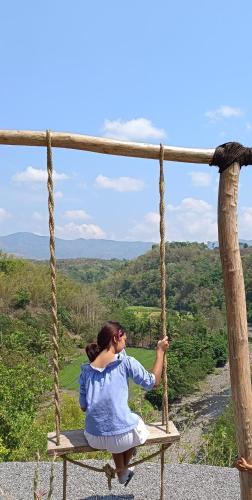 a woman sitting on a swing overlooking a valley at Tanawatu Hill in Poma