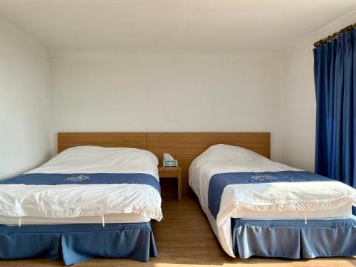 two beds in a room with blue curtains at Sweet Stay Pension in Seogwipo