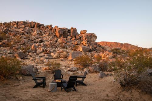 a group of chairs and a table in front of a rocky hill at Luxe Boulder Hideaway Mins to JTNP 2 Acres in Joshua Tree