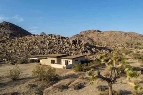 a house in the middle of a desert with mountains at Luxe Boulder Hideaway Mins to JTNP 2 Acres in Joshua Tree
