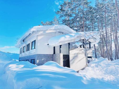 a house covered in snow in front of trees at L!fe Apartment Hakuba in Hakuba