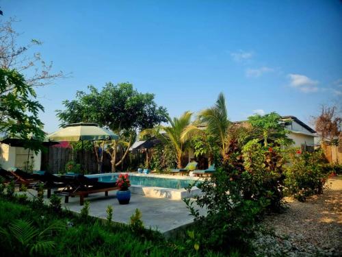 a swimming pool with benches and an umbrella in a yard at Diana Place in Paje