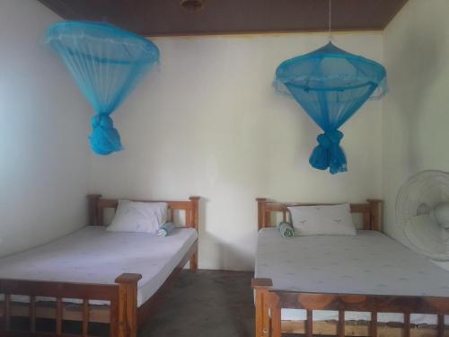two beds in a room with blue curtains at The Happy House Nature Retreat in Talakolawela