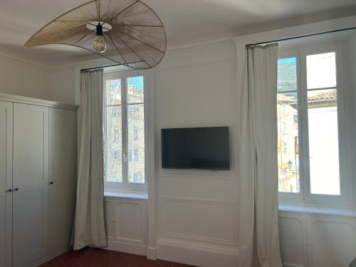 un salon avec une télévision et deux fenêtres dans l'établissement COULEUR PARFUM - VUE MER avec Balcon PARKING GRATUIT, à Grasse