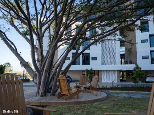 three chairs sitting around a tree in front of a building at On Park 516 At Century City in Cape Town