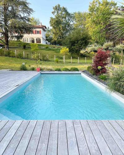 une piscine avec une terrasse en bois et une maison dans l'établissement Villa avec piscine, proche Bayonne, à Lahonce
