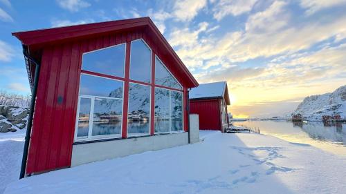 a red building in the snow next to a body of water at Ballstad Mountain Panorama in Ballstad
