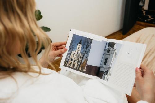 a woman sitting on a bed reading a book at DolceVita in Vinkovci