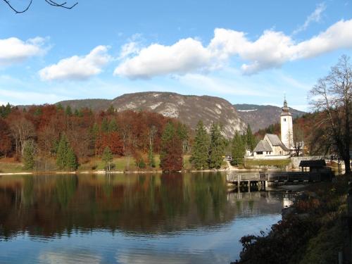 a lake with a church and a clock tower at Apartments & Hostel Bohinj in Bohinj