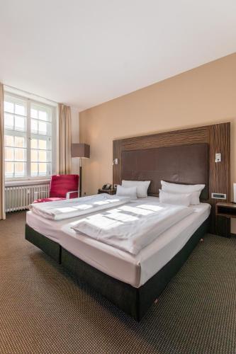 a large bed in a room with a red chair at Herzogshof - Boutique-Hotel am Dom in Regensburg