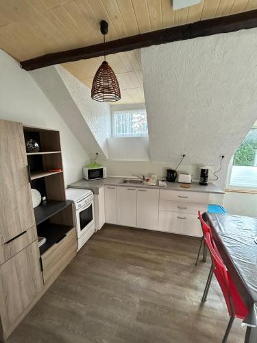 une cuisine avec des placards blancs et une table avec une chaise rouge dans l'établissement Résidence proche des plages , route de loctudy, à Pont-lʼAbbé