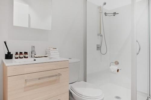 a white bathroom with a toilet and a shower at Takapuna Central Stylish 2BR Carpark Aircon in Auckland