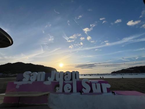 a sign on the beach with the sunset in the background at Buena Onda Backpackers in San Juan del Sur