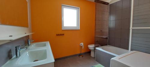 La salle de bains est pourvue de murs orange, d'un lavabo et de toilettes. dans l'établissement Loumapé, à Joyeuse