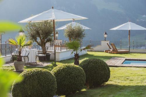 a garden with bushes and umbrellas and a swimming pool at Hotel Alpenblick Zillertal in Hippach
