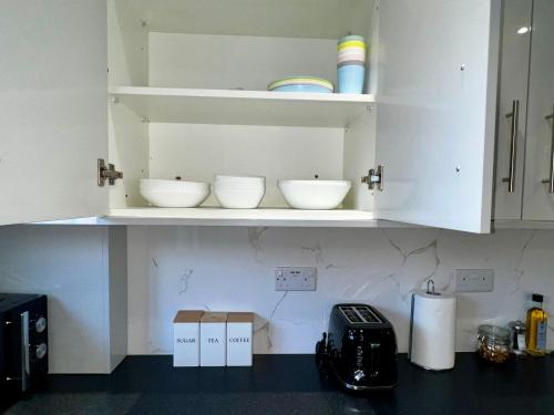 a kitchen with white cabinets with bowls on the shelf at Luxurious Cozy London Holiday Home in Cranford
