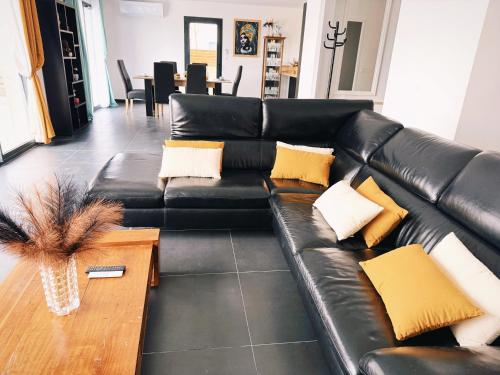 - un canapé en cuir noir avec des oreillers jaunes dans le salon dans l'établissement La maison du Canal- 9 pers- Capestang, à Capestang