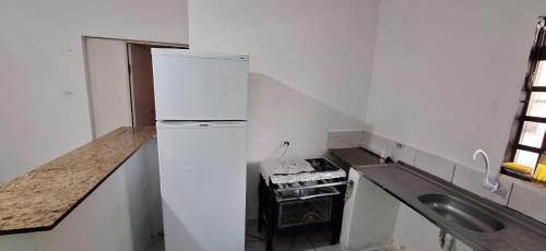 a white kitchen with a refrigerator and a sink at Quarto 1 in Várzea Grande