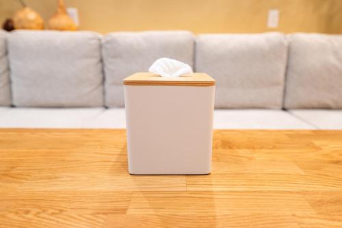 a white trash can sitting on a wooden floor with a couch at 安 Ann サウナで整う貸切の宿 USJ 万博会場近く 無料駐車場 寝室6 バスルーム4点 in Osaka