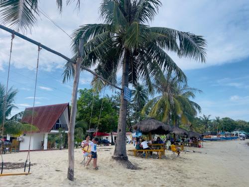a palm tree on a beach with people sitting at tables at Bolo Hills Beach Club And Residence in Alaminos