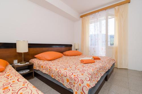 1 dormitorio con 2 camas con almohadas de color naranja y ventana en Apartments Dalmatin, en Žuljana