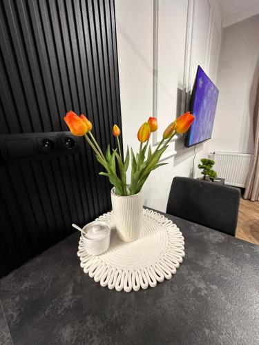 a white vase with orange flowers on a table at Apartament Z Ogrodem - Paderewskiego 22 in Bartoszyce