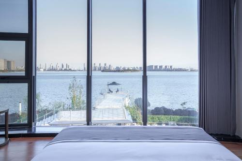 a bedroom with a large window looking out at the water at Suzhou Qingfeng Mingyue Hotel in Yinshanhunongchang