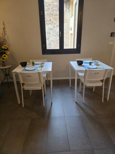 two white tables and chairs in a room with a window at Honey Rooms Ferrara in Ferrara