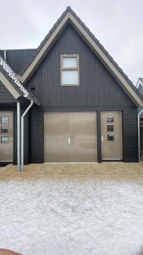 a black house with two garage doors in a driveway at B&B Smûk in Tietjerk