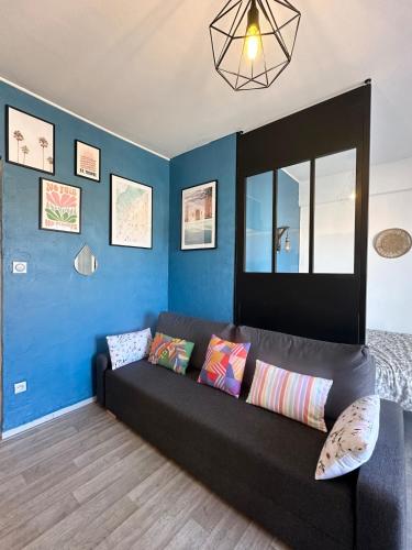 - un canapé noir dans une pièce dotée d'un mur bleu dans l'établissement Grand Studio avec Balcon au pied de la Plage Clim Wifi, à Saint Cyprien Plage