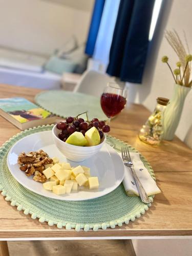 a plate with a bowl of cheese and grapes and a glass of wine at Oázis Apartmanház Balatonalmádi in Balatonalmádi