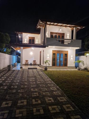 a white house at night with a brick driveway at HANSI Villa in Piliyandala