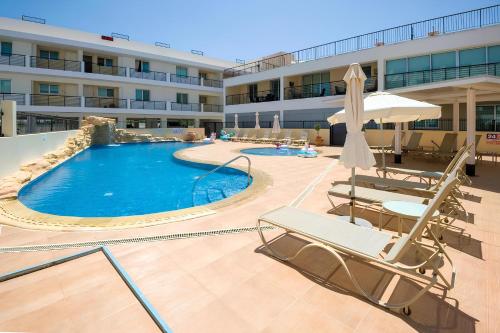 a swimming pool in a hotel with chairs and an umbrella at STAY Chromata Lagoon Apartment in Protaras