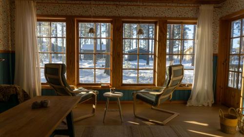 een kamer met een tafel, stoelen en ramen bij Sunshine Stuga Mörtsjön in Stugun