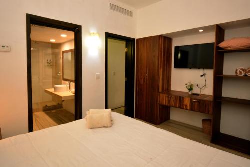ein Schlafzimmer mit einem Bett und einem TV sowie ein Badezimmer in der Unterkunft Awesome apartment at Aldea Thai Beachfront in Playa del Carmen