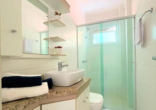 ein Badezimmer mit Waschbecken und Glasdusche in der Unterkunft 2 quartos, suíte, perto do mar, com ar e garagem! in Capão da Canoa