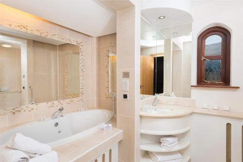 ein Badezimmer mit einer Badewanne, einem Waschbecken und einem Spiegel in der Unterkunft Delphi Resort Hotel & Spa in Leenaun