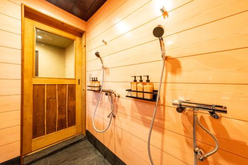 a shower in a wooden bathroom with a hose at おそば 露天風呂でリラックス ベッド7台 usjへ11分 商店街に位置するお宿 in Osaka