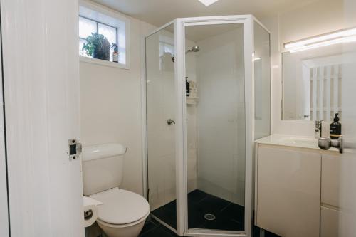 a white bathroom with a toilet and a shower at Ohana - Stylish Central Byron Studio - free secure parking in Byron Bay