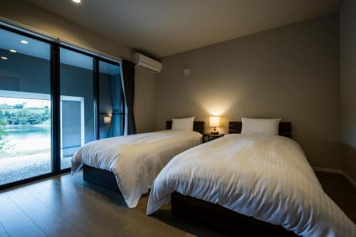 two beds in a bedroom with a large window at Seaside Villa N Plus in Mitsugoe