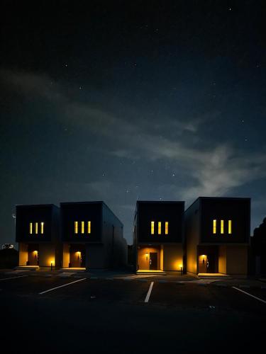 two black buildings with lights in a parking lot at night at Seaside Villa N Plus in Mitsugoe