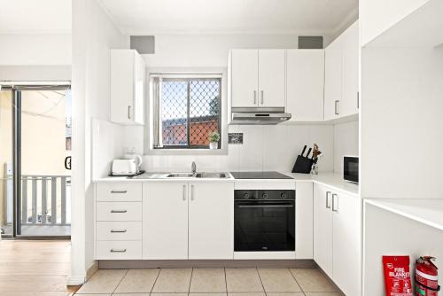 a white kitchen with white cabinets and a black dishwasher at Double Room - Prime location - Convenient Spot in Auburn - Shared Bathroom in Sydney