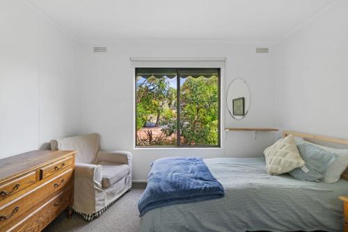 a bedroom with a bed and a chair and a window at Little Pier Cottage in Inverloch
