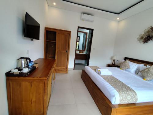 a bedroom with a bed and a desk and a television at Kubera Villa Kemenuh by Prasi in Ubud