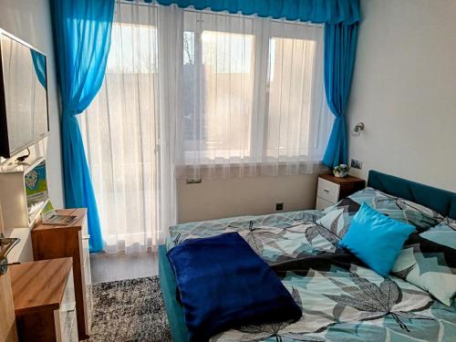 a bedroom with a bed with blue sheets and blue curtains at Apartman Roberto in Hajdúszoboszló