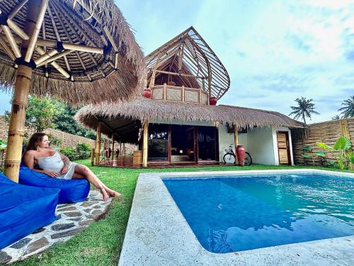 a woman sitting on a couch next to a swimming pool at Villa Kesambi in Gili Air