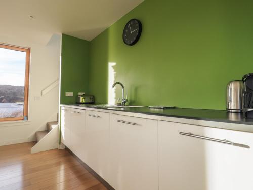a green kitchen with white cabinets and a clock on the wall at Loch View in Breaclete