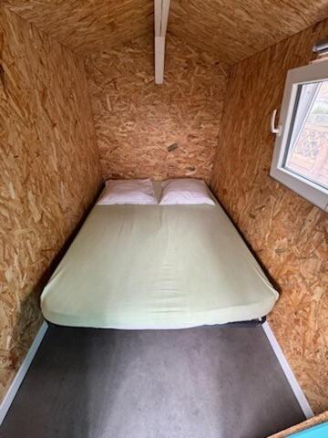 Cette petite chambre comprend un matelas vert et une fenêtre. dans l'établissement Cabane des randonneurs, jardin, Bassin d'Arcachon, au Teich