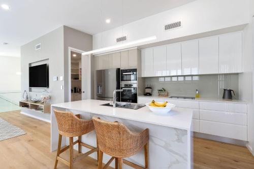 a kitchen with white cabinets and a counter with chairs at Rooftop Alexandra Headland in Alexandra Headland