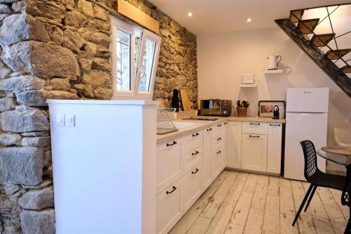 - une cuisine avec des placards blancs et un mur en pierre dans l'établissement Duplex rénové U Fragnu, à Prunelli-di-Fiumorbo